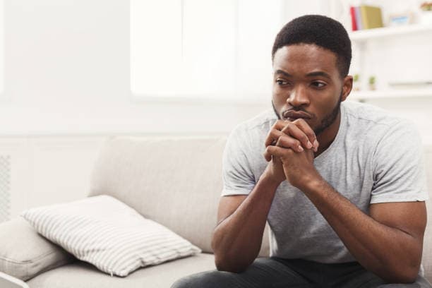 A man sitting on a sofa looking worried with his hands clasped