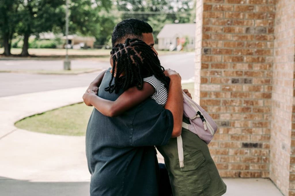 A parent hugging a child with a backpack at the doorway