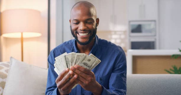 A smiling man sitting on a sofa holding cash